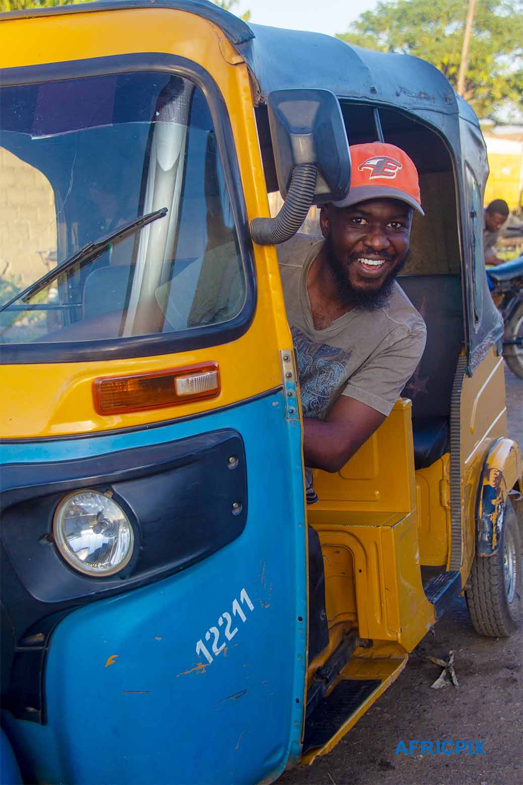 A happy African man riding a tricycle, Keke , smiling with joy as he enjoys the ride,Portrait wearing a cap